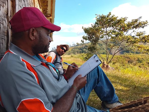 A facilitator recording notes during a community field visit. Catholic Diocese of Mendi, Lower Mendi Parish, Southern Highlands. July 2026.