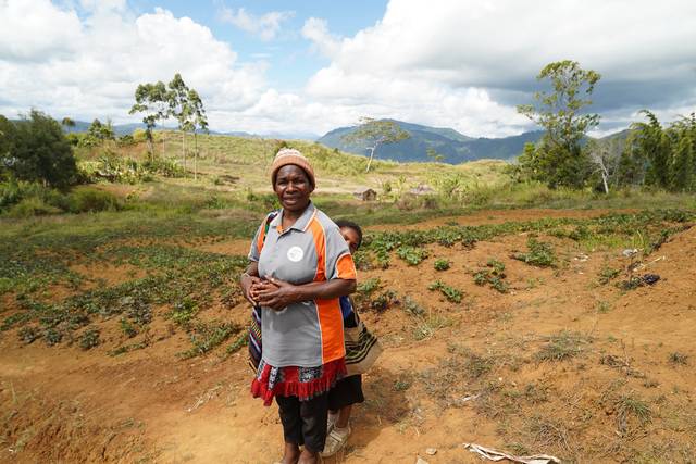 Margaret Lord, a Community Curriculum facilitator, stands in a Highlands garden with a child at her back.